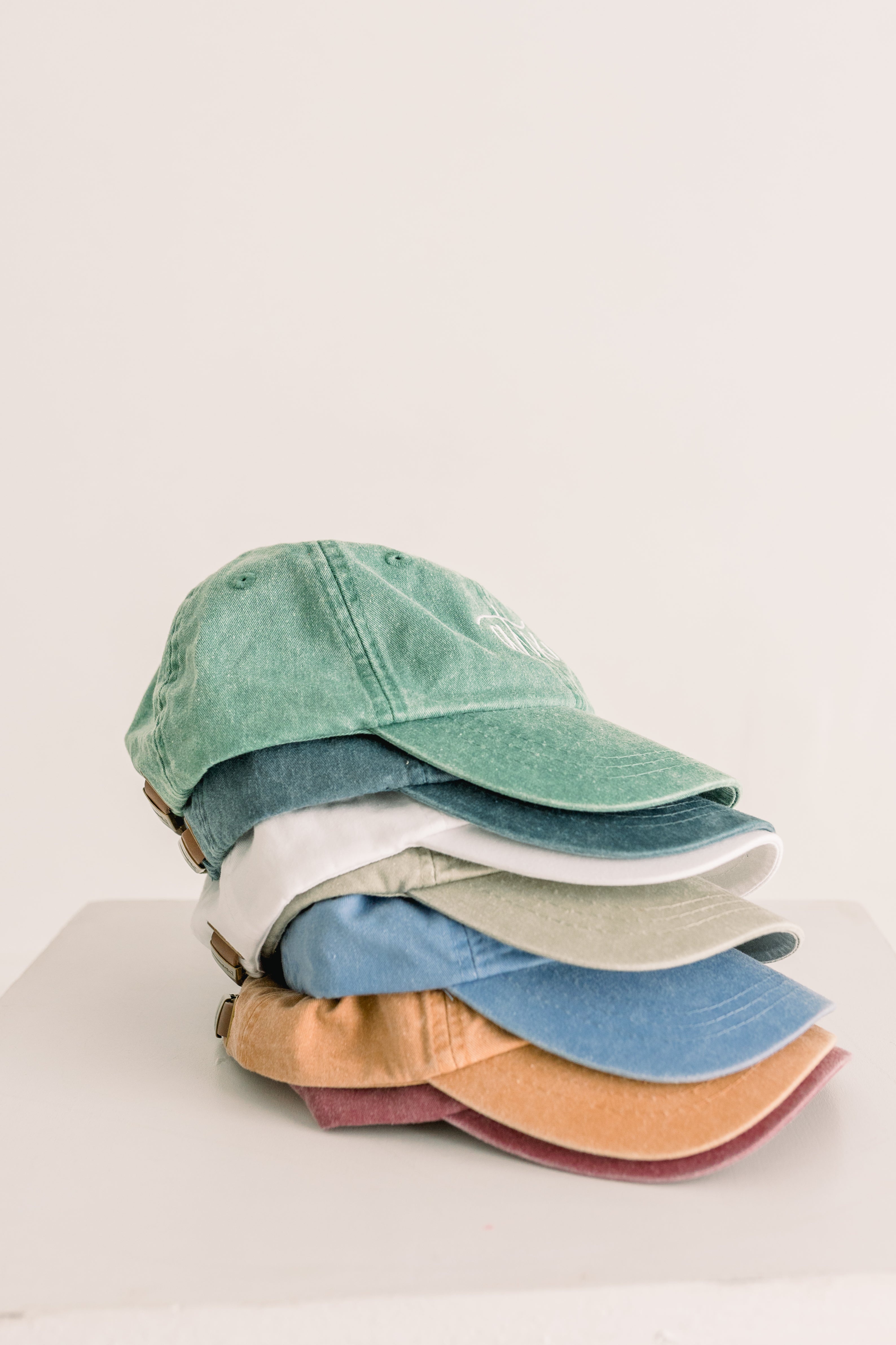Stack of colorful baseball caps on a white surface with a light gray background